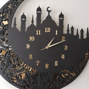 May include: Black and gold clock with a crescent moon and mosque silhouette design. The clock face has Roman numeral markings and a gold-colored hour and minute hand.