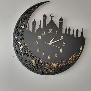 May include: Black clock with gold numbers and a crescent moon design. The clock features a silhouette of a mosque with minarets.