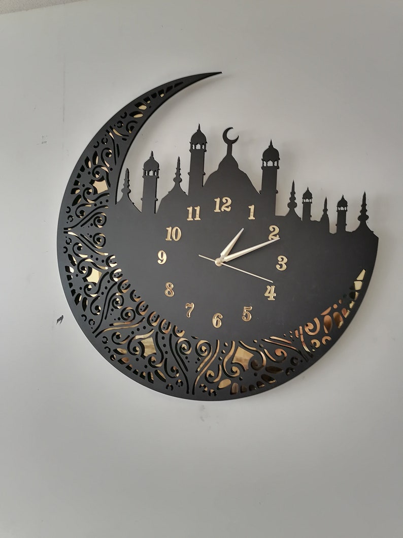 May include: Black clock with gold numbers and a crescent moon design. The clock features a silhouette of a mosque with minarets.