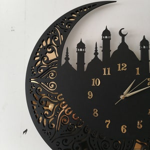 May include: Black and gold wall clock with a crescent moon design and a mosque silhouette. The clock face has Roman numerals and gold hands.