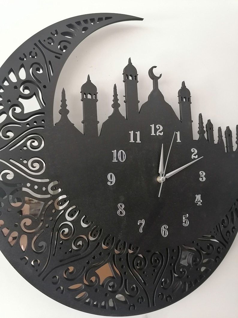 May include: Black clock with a crescent moon and mosque silhouette design. The clock face has silver numbers 1 through 12 and silver hands.