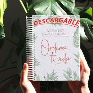 Puede incluir: Una agenda blanca con espiral. La portada tiene un diseño de hojas verdes y el texto "DESCARGABLE MI PLANNER DIARIO COTIDIANO Ordena tu vida".