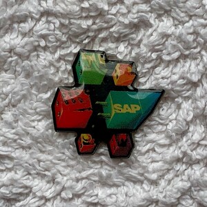 Puede incluir: Un pin colorido con un logotipo de bloques entrelazados y la palabra "SAP" en letras blancas sobre un bloque verde.