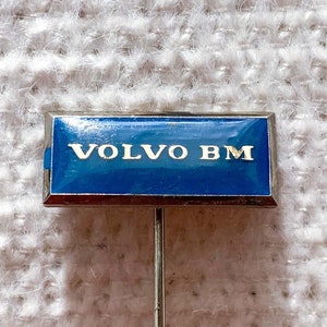 May include: A blue and silver pin with the text "VOLVO BM" on it.