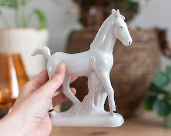 Puede incluir: Figurita de caballo de porcelana blanca con detalles negros. El caballo está de pie sobre una base con un diseño texturizado.