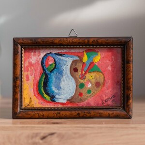 May include: A framed painting of a blue pitcher and a paint palette with colorful paint splatters on a red background. The painting is signed "S. Kenis 1977".