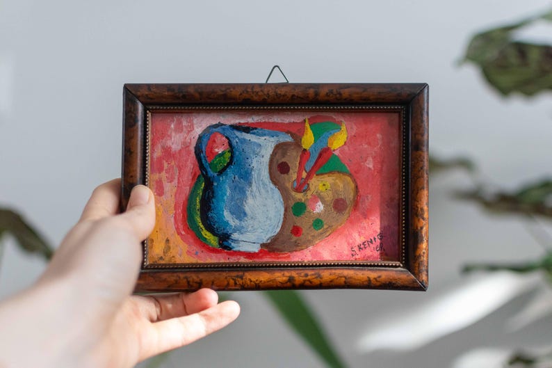 May include: A framed painting of a blue pitcher and a colorful paint palette on a red background. The painting is signed "S. Kenis 67".