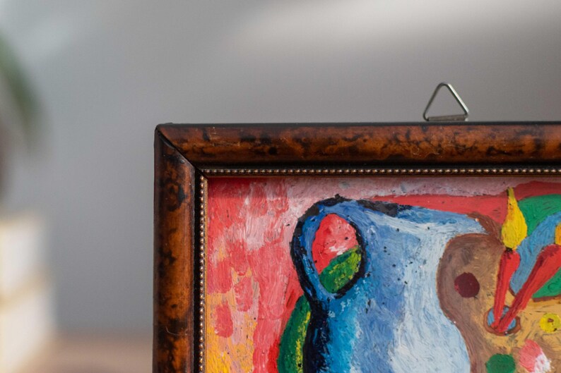May include: A framed abstract painting with a blue, red, yellow, and green color scheme. The painting depicts a still life with a vase and other objects.