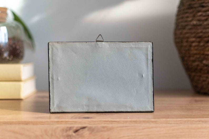 May include: A black picture frame with a white mat and a metal hanging hook on the back.