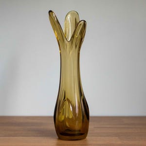 May include: A brown glass vase with a unique, organic shape. The vase has a wide opening at the top and a narrow base.