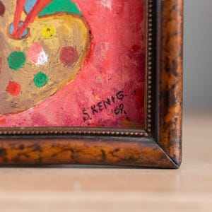 May include: A framed painting of a palette with colorful paint splatters on a red background. The painting is signed "S.KENIG - 169."