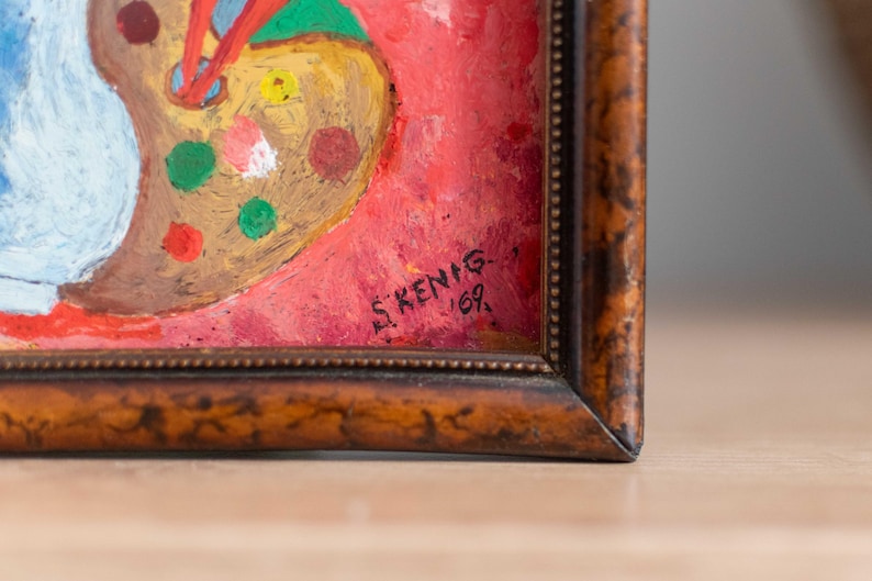 May include: A framed painting of a palette with colorful paint splatters on a red background. The painting is signed "S.KENIG - 169."