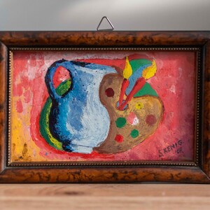 May include: A framed painting of a blue pitcher and a paint palette with paintbrushes on a red background. The painting is signed "S. Kenig 69".