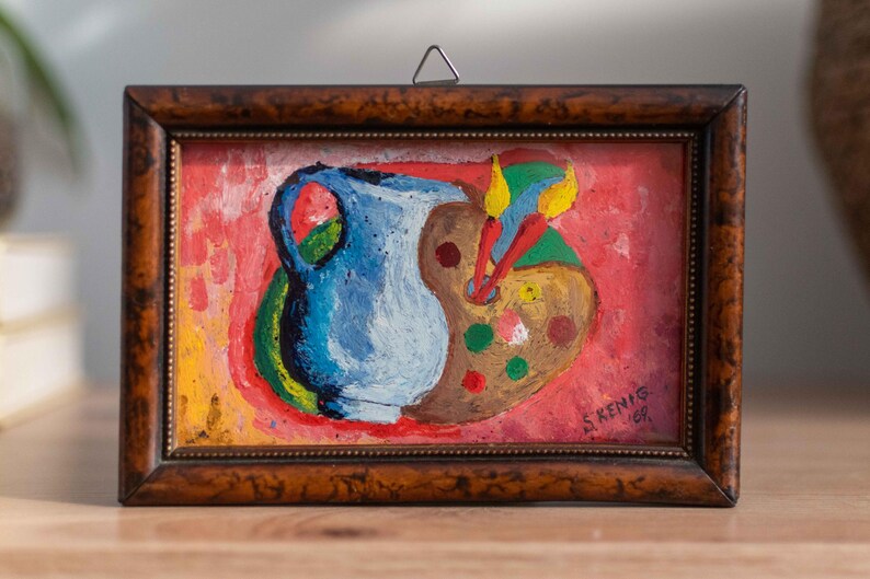 May include: A framed painting of a blue pitcher and a paint palette with paintbrushes on a red background. The painting is signed "S. Kenig 69".