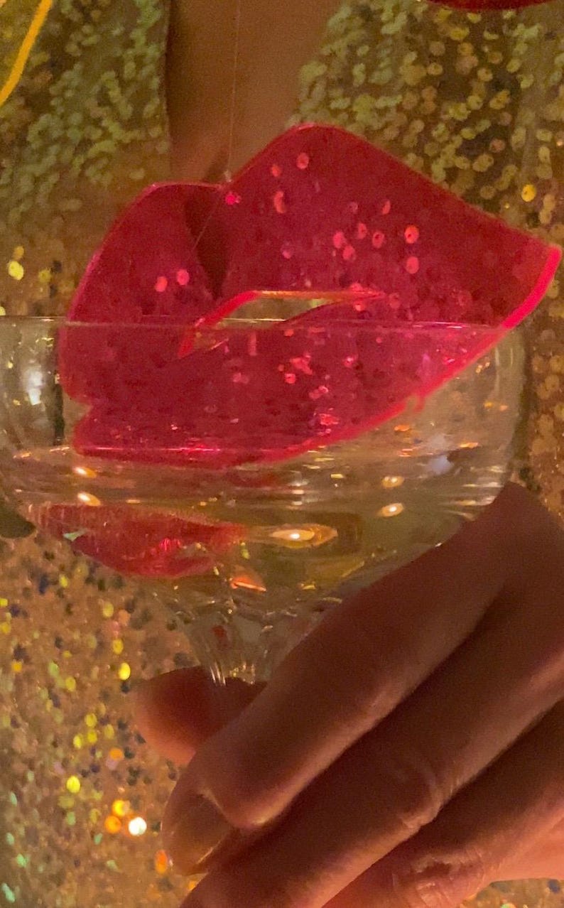 Pu&ograve; includere: Uno stampo per ghiaccio a forma di labbra rosa con glitter in un bicchiere trasparente pieno d'acqua.