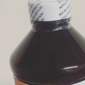 May include: A dark brown glass bottle with a white cap. The cap has a tamper-evident seal with the text "SEALED FOR YOUR PROTECTION" printed on it.