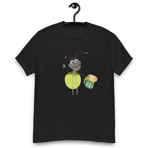 Puede incluir: Camiseta negra con un diseño de luciérnaga de dibujos animados sosteniendo una jarra de cerveza verde. La luciérnaga tiene un abdomen amarillo, cara verde y antenas rojas. La camiseta está colgada de una percha negra.
