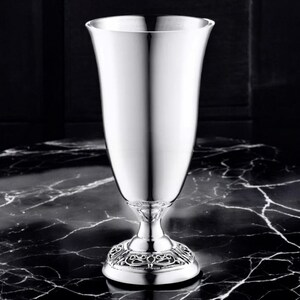 May include: A silver vase with an ornate base and a smooth, polished finish. The vase is tall and slender, with a wide opening at the top.