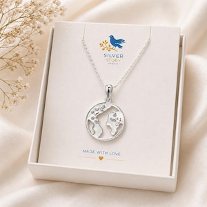 May include: A silver-colored necklace with a globe pendant, presented in a white gift box. The pendant features a detailed outline of the continents. The box has the text "SILVER STORY DESIGN" and "MADE WITH LOVE".