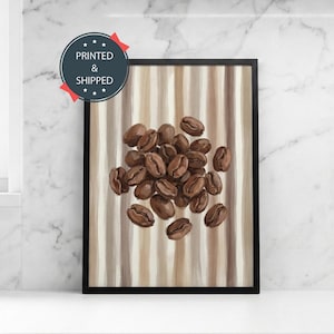 May include: A framed art print featuring a cluster of roasted coffee beans. The beans are a rich brown color and are set against a background of vertical beige and brown stripes. The frame is black. The print has a circular sticker that says "PRINTED & SHIPPED".