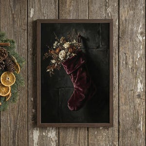 May include: A framed print featuring a burgundy velvet Christmas stocking overflowing with dried flowers and foliage. The artwork is set against a dark background, creating a striking contrast. The frame is a dark brown color.