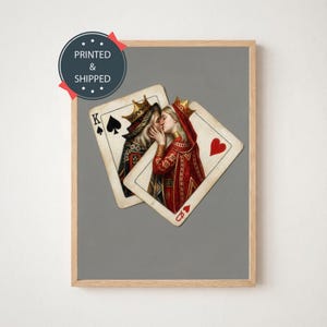 May include: Framed print featuring two playing cards, a King of Spades and a Queen of Hearts, depicting a romantic scene. The King and Queen are kissing. The print is set against a gray background, with the text "PRINTED & SHIPPED" in a circle.