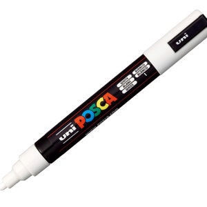 May include: White Uni Posca paint marker with a black cap and a black label that says "Uni Posca" and "www.posca.com". The label also has the words "White", "Blanc", "Bianco", "Blanco", and "Weiss" written in different languages. The marker is 13.5 cm long.
