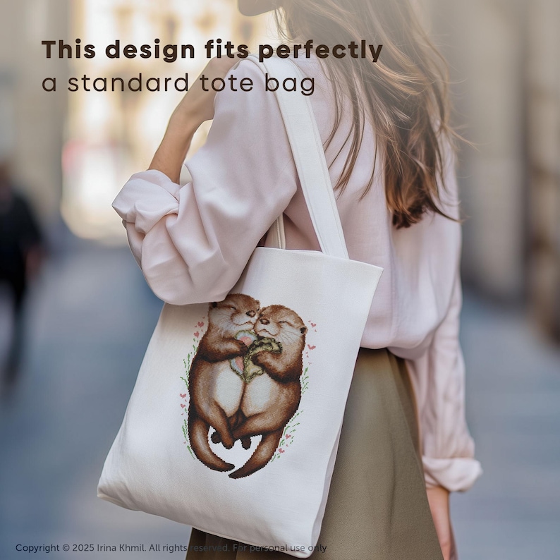 May include: A white tote bag with a design of two otters hugging. The otters are brown and have pink noses. The design is surrounded by small pink flowers and green leaves.
