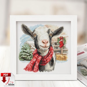 May include: A framed cross-stitch of a goat wearing a red scarf. The goat has black and white markings and is smiling. The background includes a Christmas tree, a fence, and a wreath.