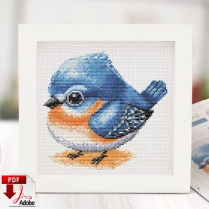 May include: A cross-stitch of a bluebird with a blue head and wings, orange chest, and black beak. The bird is perched on a tan surface, set within a white frame. The image is a PDF download.