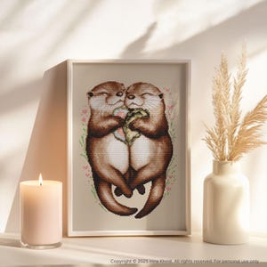 May include: Two brown otters cuddling and holding a heart-shaped object. The otters are surrounded by pink flowers and green leaves.