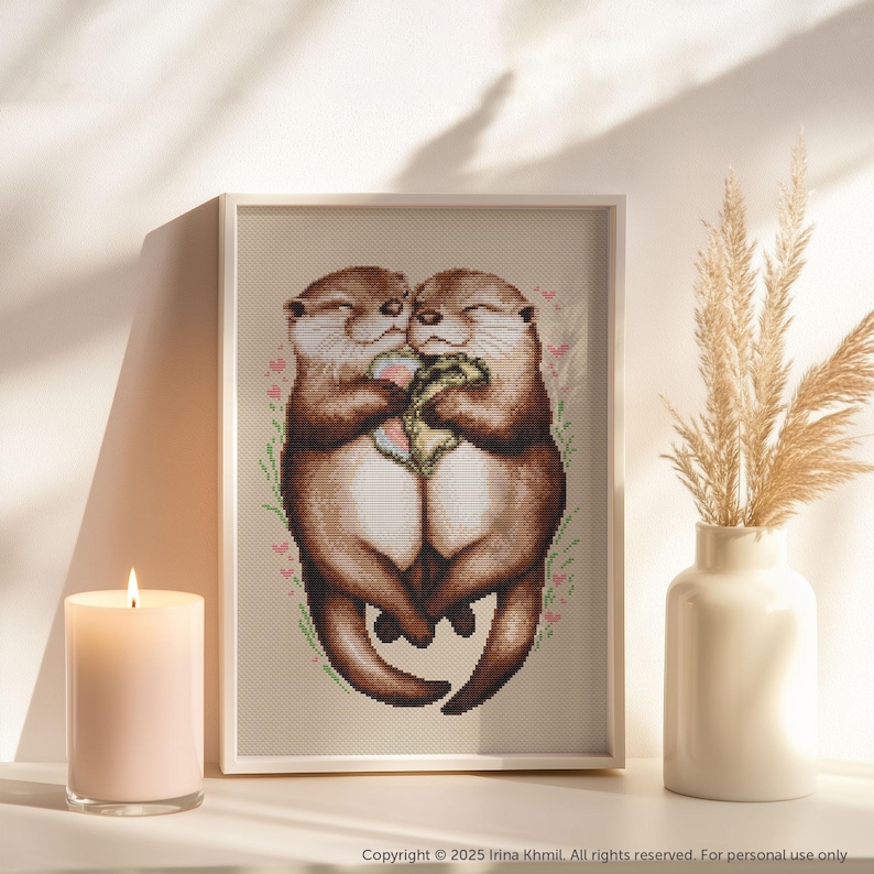 May include: Two brown otters cuddling and holding a heart-shaped object. The otters are surrounded by pink flowers and green leaves.
