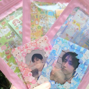 May include: A collection of pink plastic bags filled with colorful stickers and photo cards. The stickers feature various cartoon characters and designs. Two photo cards are visible, each with a person's image and a decorative frame.