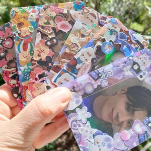 May include: A collection of decorative photo cards with colorful, cartoon-themed stickers. The cards feature various designs, including bears, bunnies, and other cute characters. One card displays a photo framed with purple stickers and embellishments.