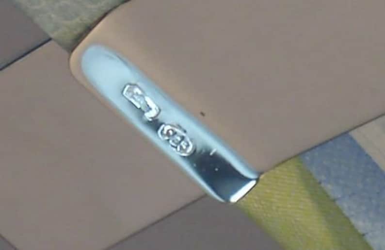 May include: Close-up of a silver metal tag with the inscription "925" on a brown leather surface.