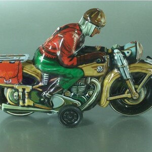 K&ouml;nnte beinhalten: Ein Vintage-Blechspielzeug-Motorrad mit einem Fahrer in einer roten Jacke und gr&uuml;nen Hosen. Das Motorrad ist braun und goldfarben mit schwarzen R&auml;dern und einem Beiwagen. Das Motorrad hat ein Nummernschild mit der Aufschrift "N-JW 14".