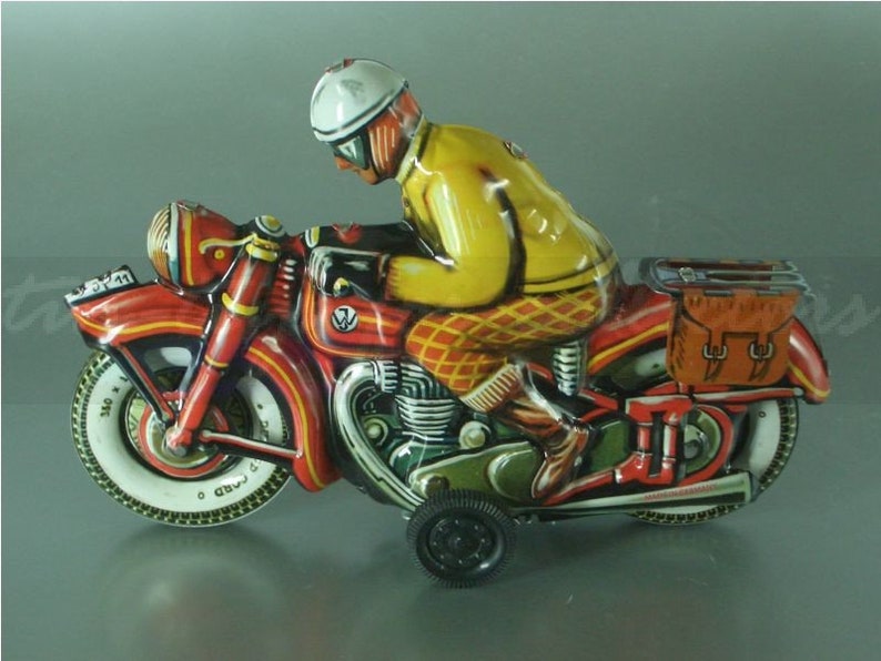 K&ouml;nnte beinhalten: Ein rotes und schwarzes Spielzeugmotorrad mit einem Fahrer, der einen gelben und wei&szlig;en Helm tr&auml;gt. Das Motorrad hat eine braune Satteltasche und einen wei&szlig;en Reifen mit schwarzer Beschriftung "340 x 120".