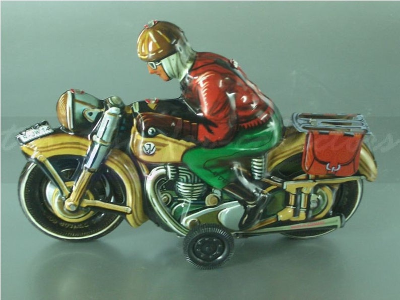 K&ouml;nnte beinhalten: Ein vintage Blechspielzeug-Motorrad mit einem Fahrer, der einen braunen Helm und eine rote Jacke tr&auml;gt. Das Motorrad ist gelb und gr&uuml;n mit einer roten und braunen Satteltasche.