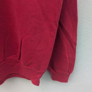 May include: A red sweatshirt with long sleeves and a ribbed cuff. The sweatshirt is made of a soft, comfortable fabric.