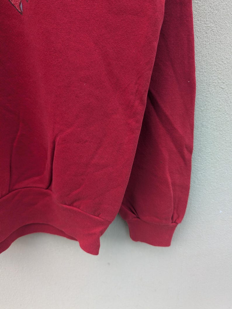 May include: A red sweatshirt with long sleeves and a ribbed cuff. The sweatshirt is made of a soft, comfortable fabric.