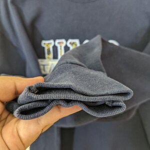Peut inclure: Un sweat-shirt bleu marine avec un motif blanc et noir repr&eacute;sentant le mot "Texas" sur un th&egrave;me de baseball. Le sweat-shirt a une bordure c&ocirc;tel&eacute;e.