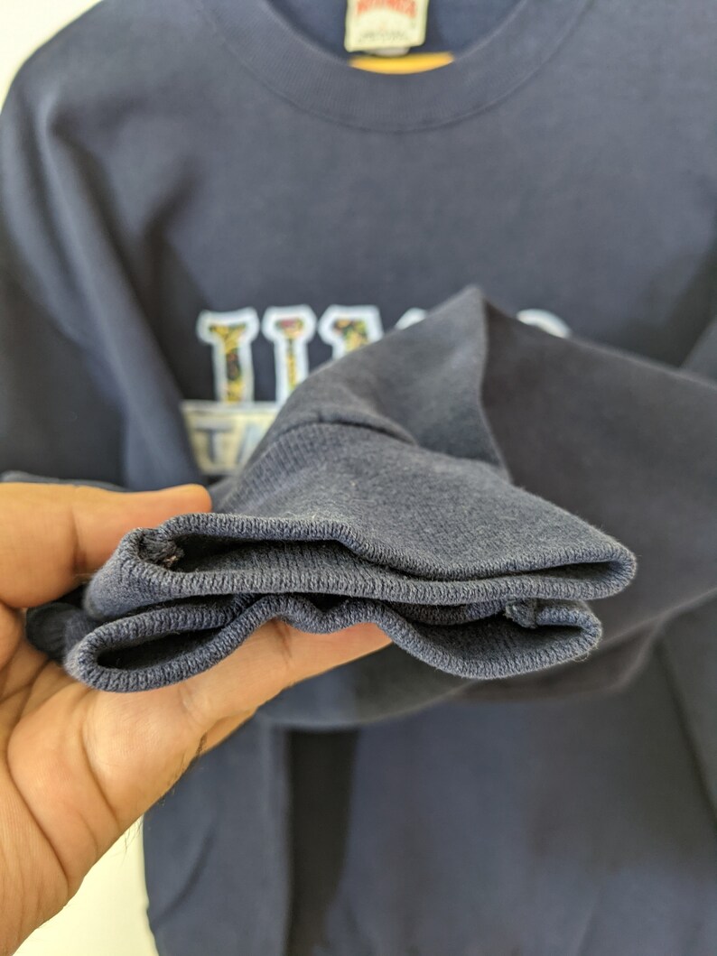 Peut inclure: Un sweat-shirt bleu marine avec un motif blanc et noir repr&eacute;sentant le mot "Texas" sur un th&egrave;me de baseball. Le sweat-shirt a une bordure c&ocirc;tel&eacute;e.