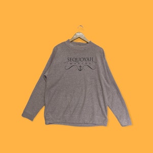 Op de afbeelding: Een grijs sweatshirt met lange mouwen met de tekst "Sequoyah Marina" en een ankersymbool gedrukt op de voorkant.