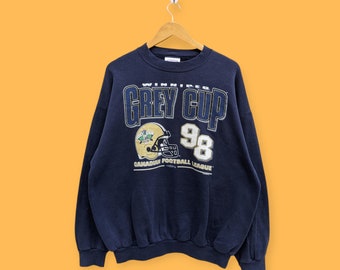 May include: A navy blue sweatshirt with a gold and white graphic of a football helmet and the text "Winning Grey Cup 98 Canadian Football League".