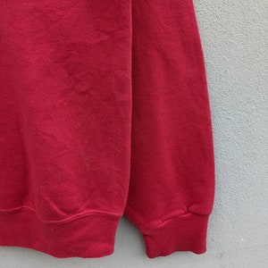 May include: Red sweatshirt with a black and white embroidered logo on the front. The sweatshirt has a ribbed cuff and hem.