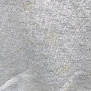 May include: Close-up of a gray sweatshirt fabric with a few light brown stains.