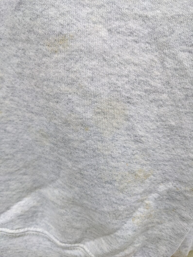 May include: Close-up of a gray sweatshirt fabric with a few light brown stains.