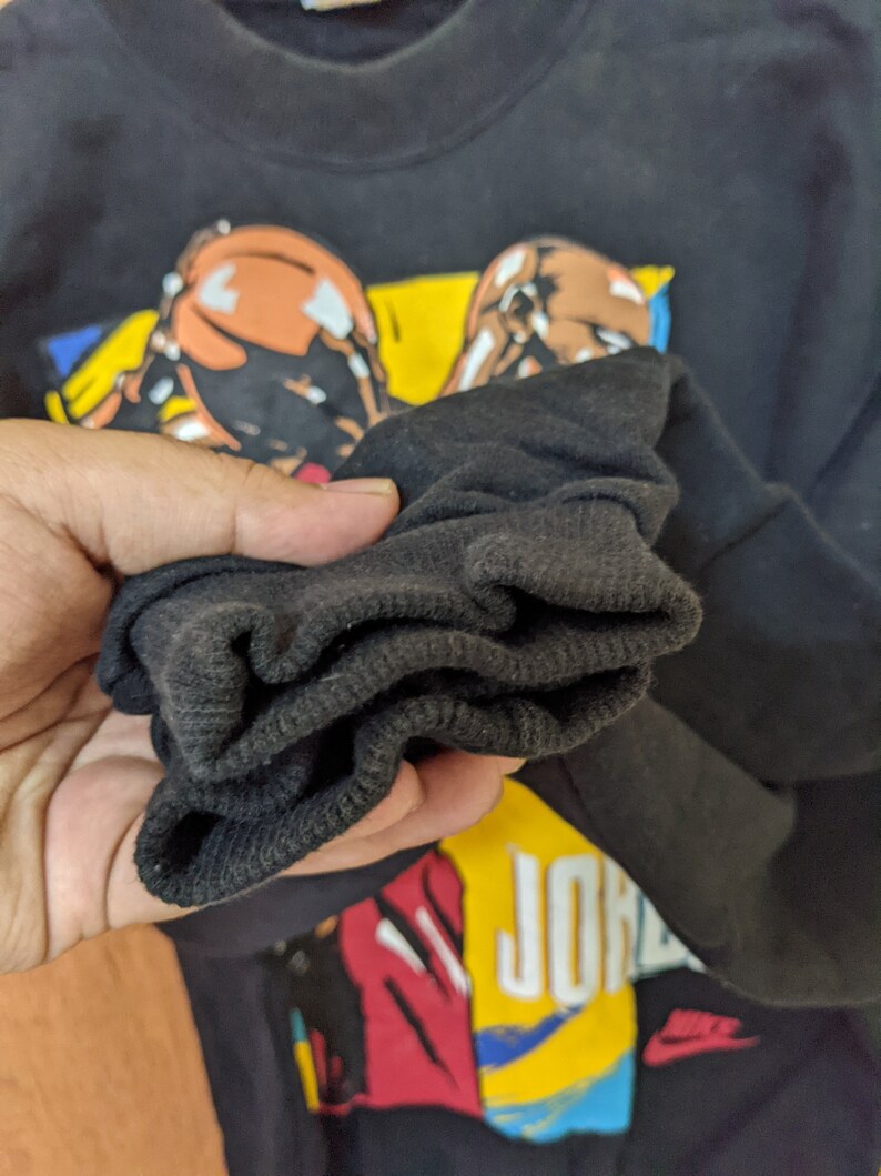 May include: Black long-sleeve shirt with a graphic print of two basketball players and the text "Air Jordan". The shirt has a ribbed cuff.
