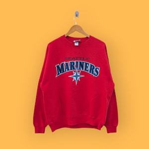 May include: Red sweatshirt with a blue and white Seattle Mariners logo. The logo features the team name and a star.