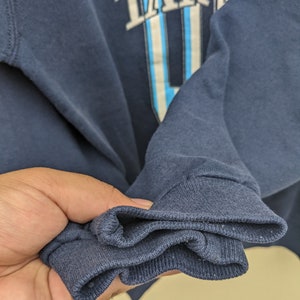 May include: Close-up of the navy blue cuff of a sweatshirt. The cuff is folded over three times, showing the soft, knitted fabric.